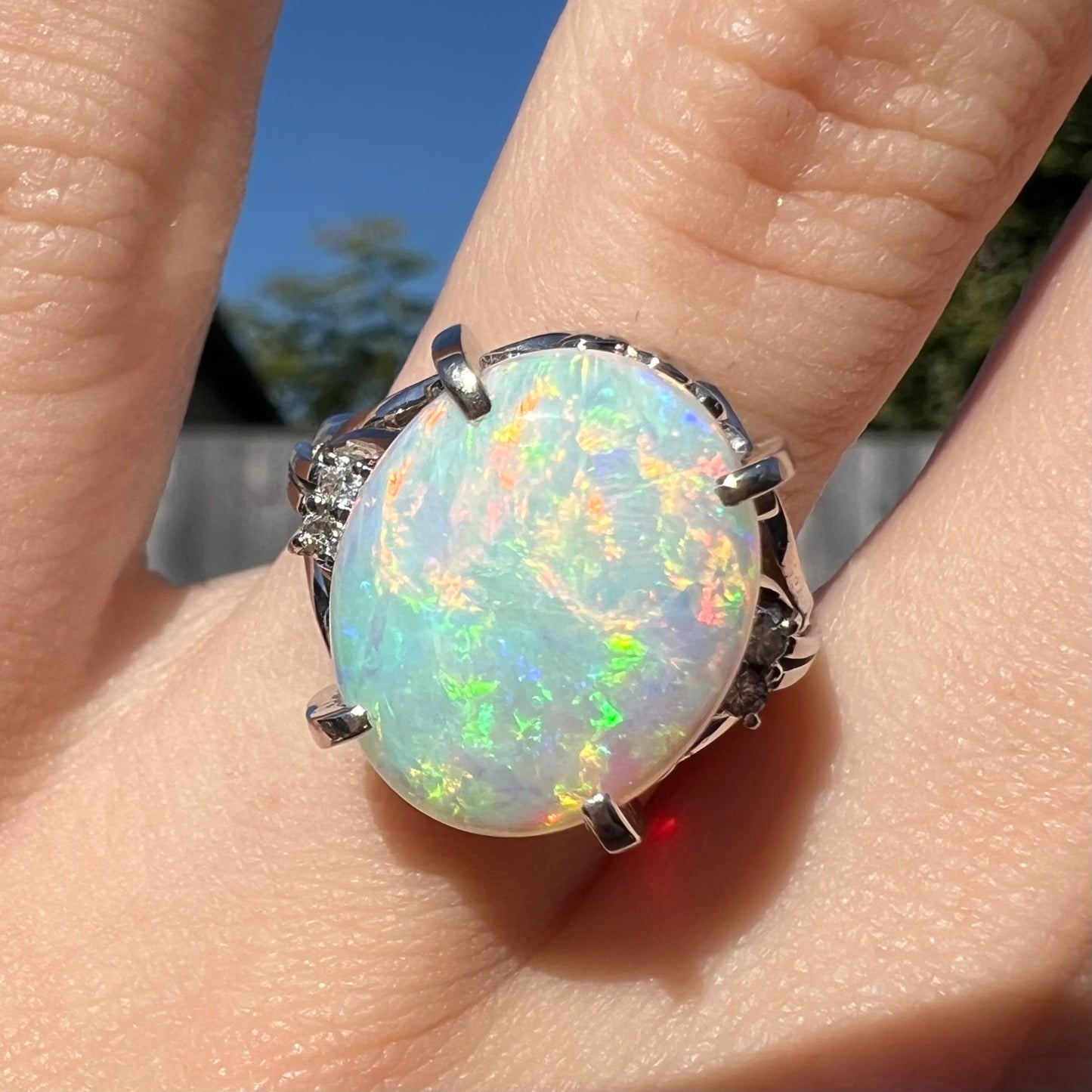 A 4.83ct platinum opal engagement ring with diamond accents worn on a finger in sunlight.