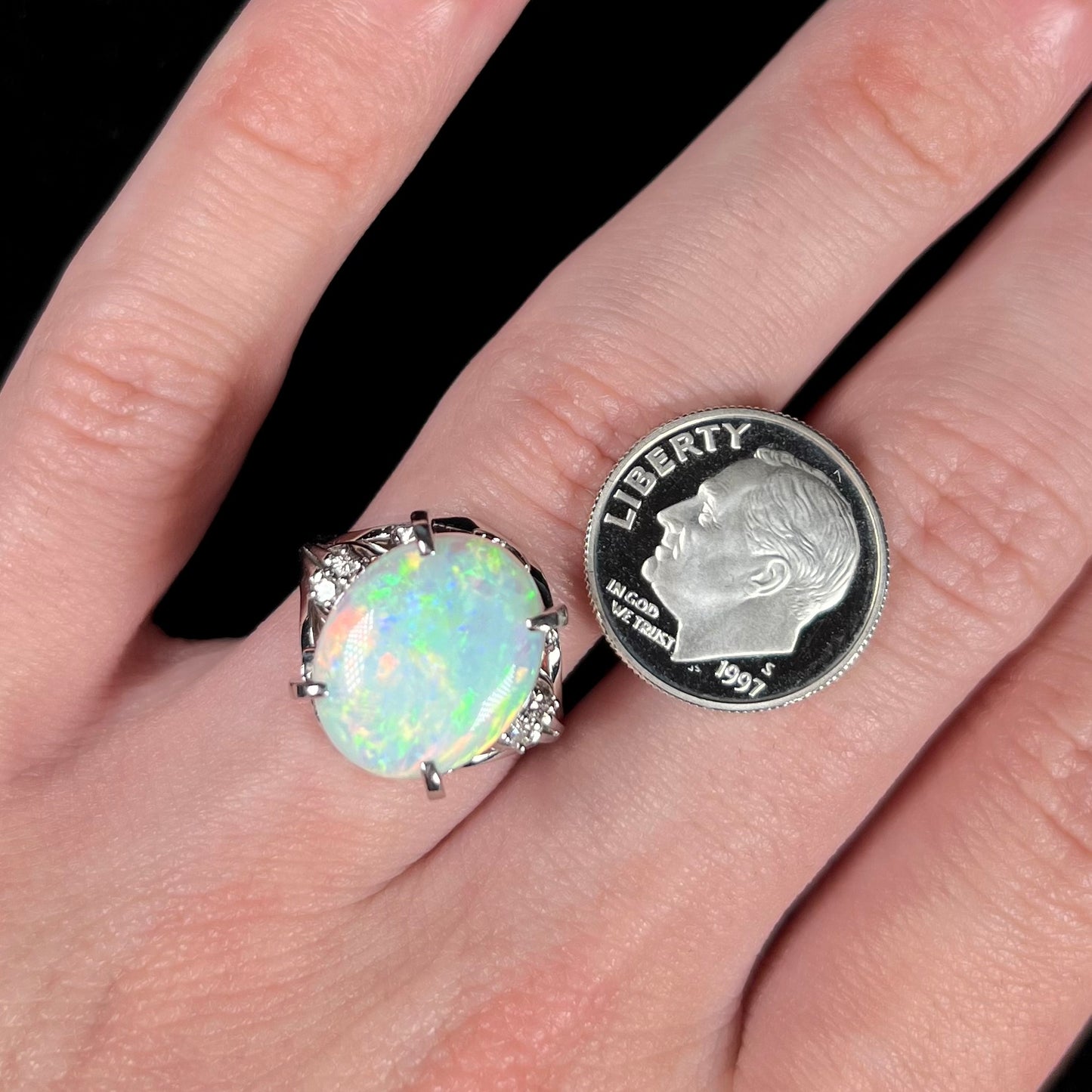 A 4.83ct opal and diamond ring, worn on a hand next to a dime coin for scale.