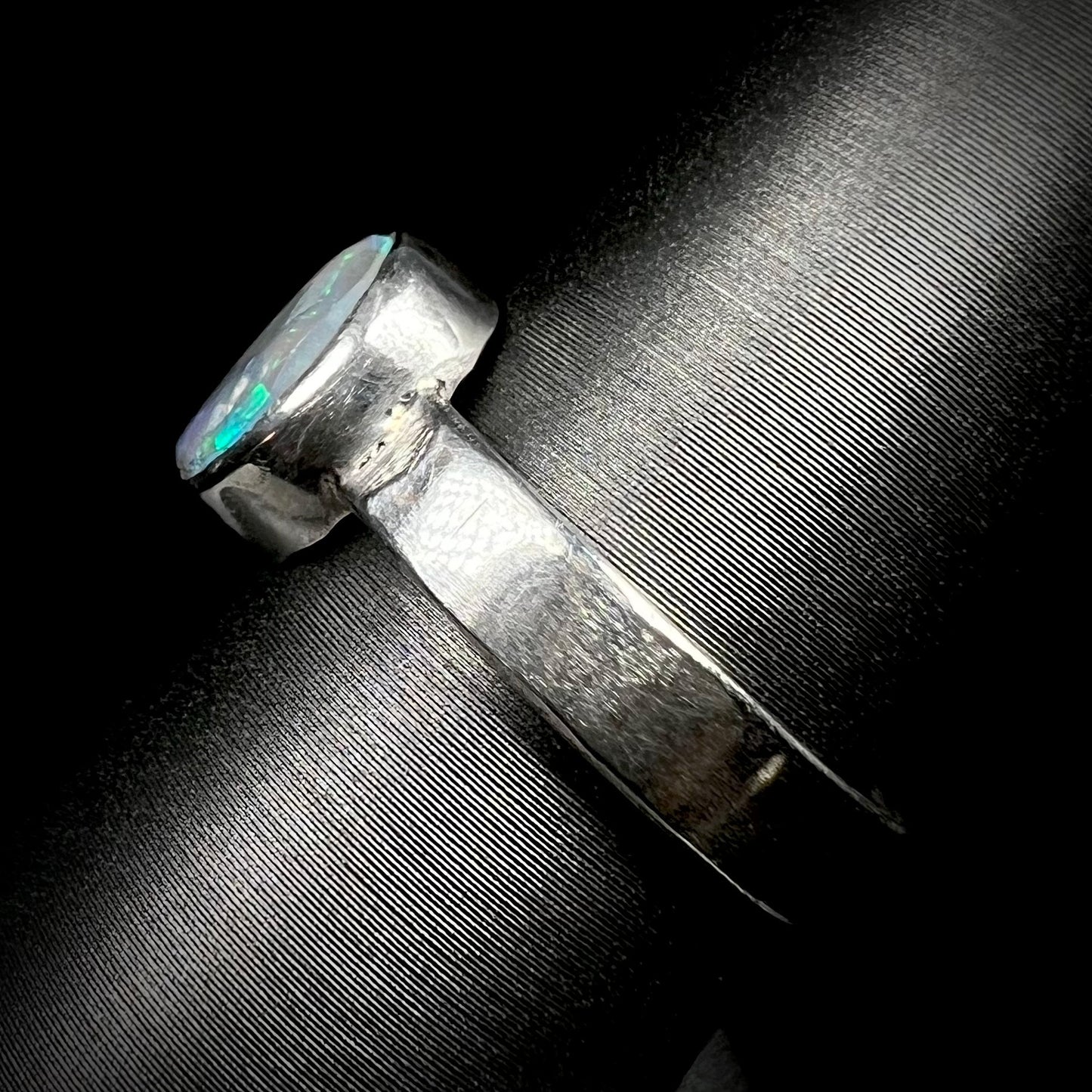 Side view of a sterling silver bezel-set opal ring on a ring display.  The ring's unisex 4mm wide shank is in focus.