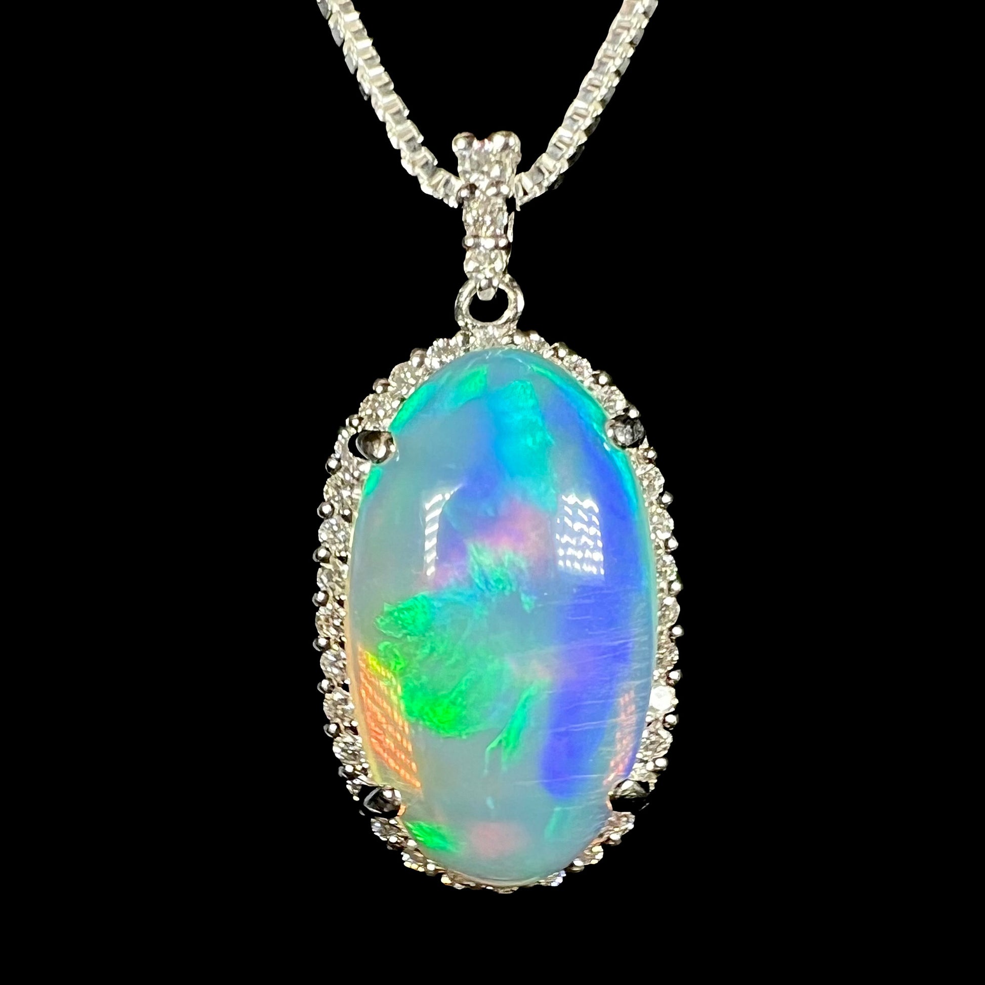 A 5.20ct Ethiopian jelly crystal opal and diamond halo pendant made from platinum, shown on a chain against a black background.