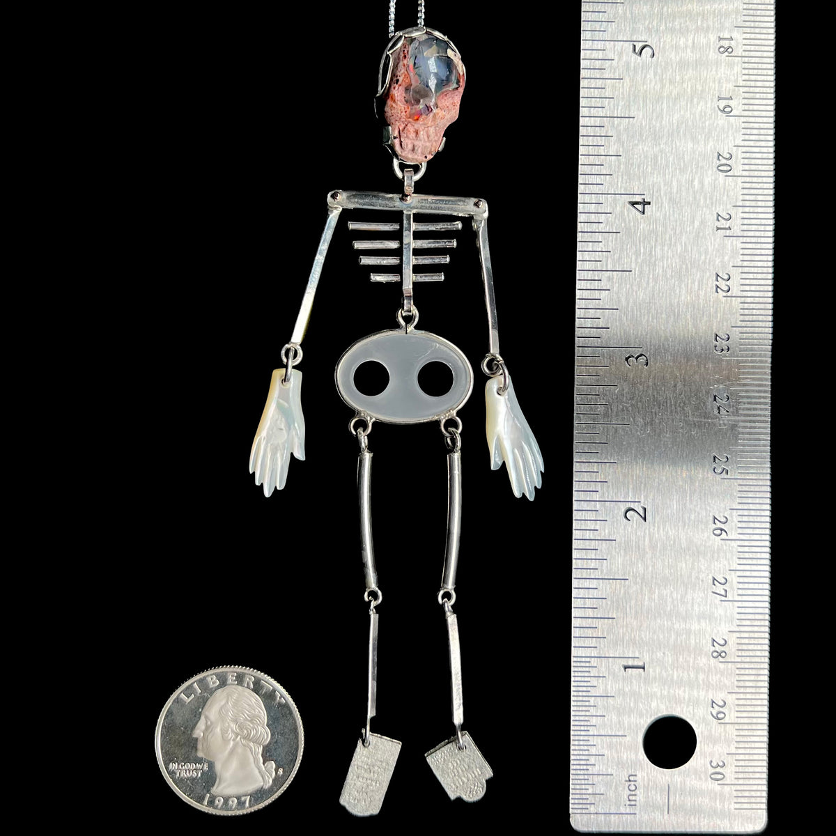 5 inch-long sterling silver skeleton statement pendant with carved cantera opal skull shown between US quarter coin and ruler for scale