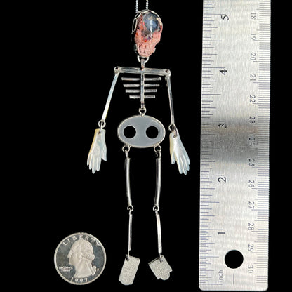 5 inch-long sterling silver skeleton statement pendant with carved cantera opal skull shown between US quarter coin and ruler for scale