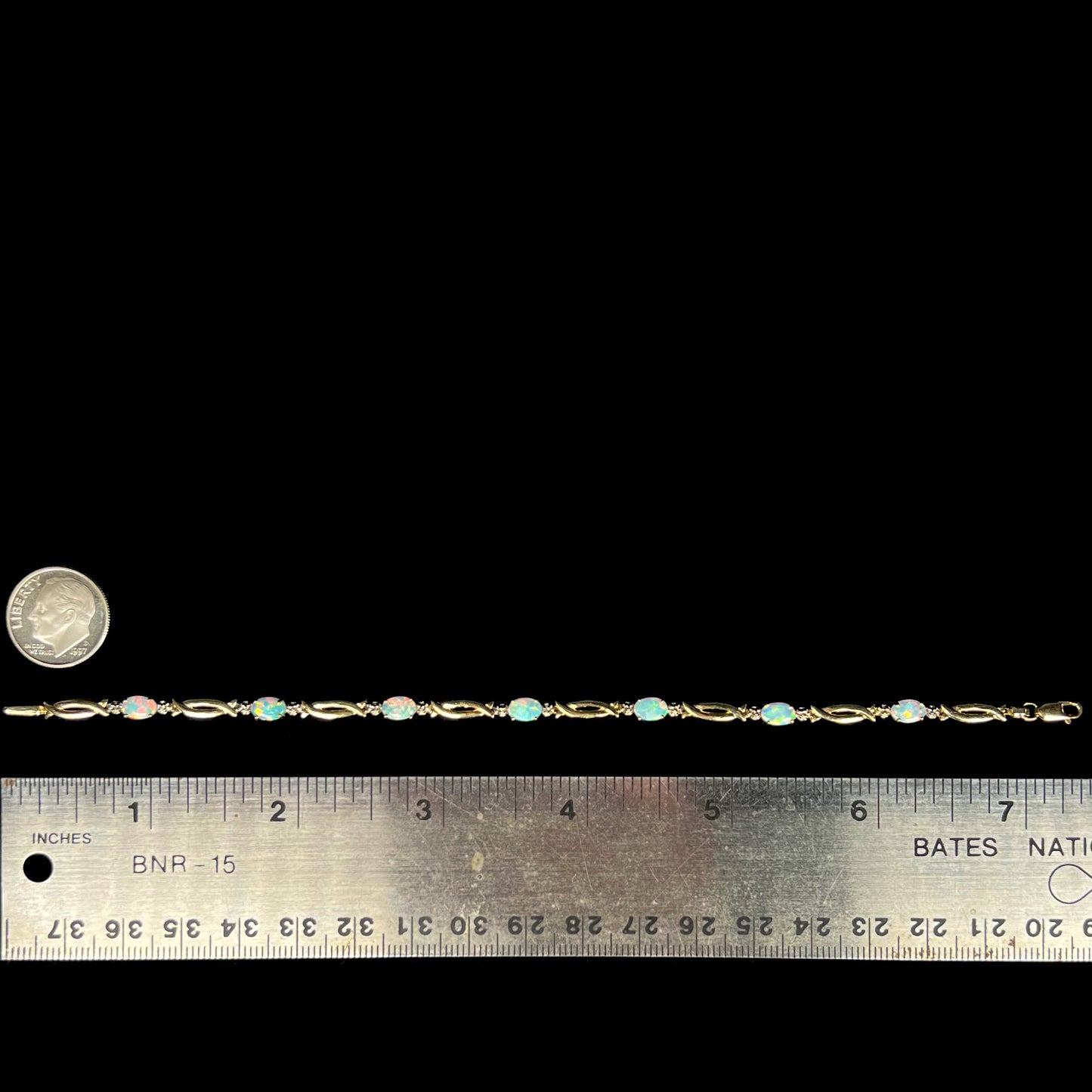 7.25 inch-long 10k gold lab-created opal and diamond bracelet shown on black background next to ruler and US dime coin for scale.