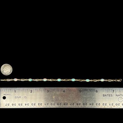 7.25 inch-long 10k gold lab-created opal and diamond bracelet shown on black background next to ruler and US dime coin for scale.