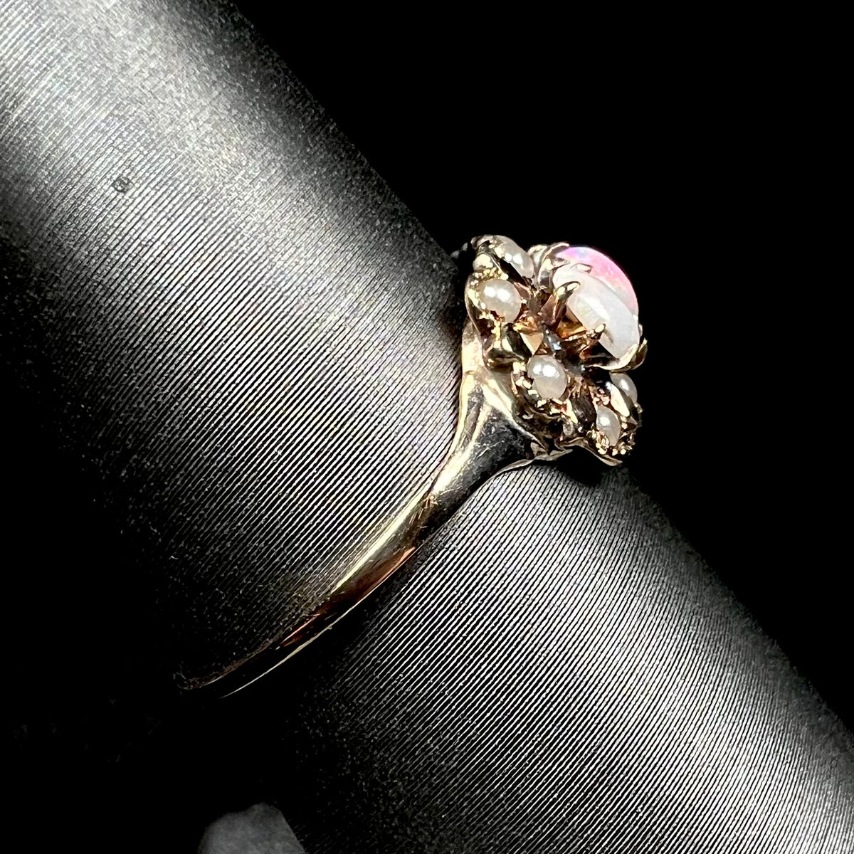 A delicate antique 9k gold opal and seed pearl ring shown on ring display from the side view, its shank in focus