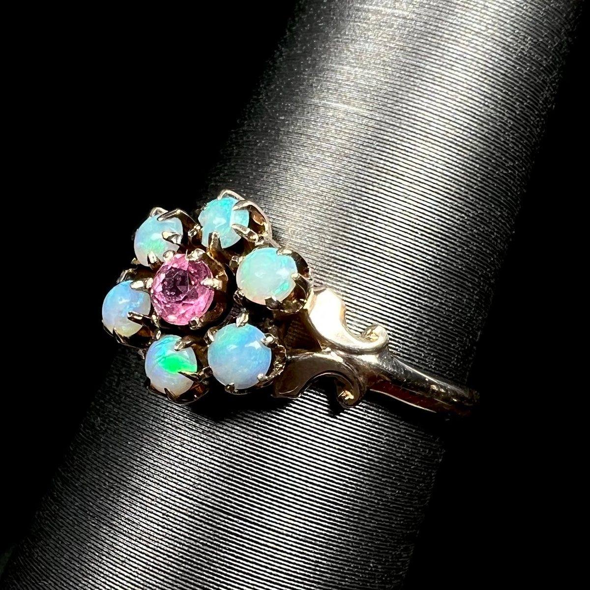 Angled close-up of antique Victorian 9k gold Hungarian opal and pink tourmaline flower ring, shown on ring display