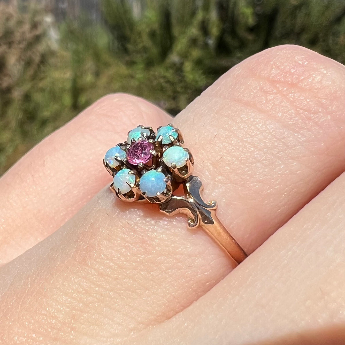 Angled view of 9k gold Hungarian opal and pink tourmaline ring from Victorian era, worn on finger under sunlight