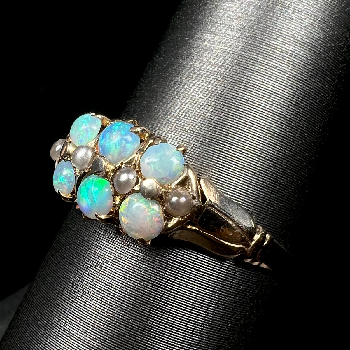 Angled close-up of antique 9k gold opal and pearl ring with Victorian design, shown on ring display