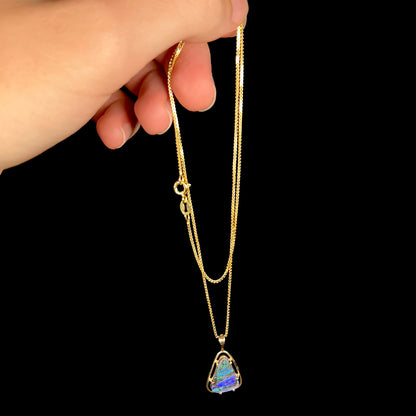 A dainty Duck Creek opalized wood necklace in 9k gold, shown dangled from a hand by its chain.