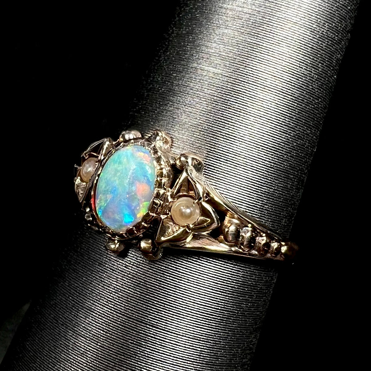 Angled close-up of dainty 9k gold Victorian opal and pearl ring on ring display