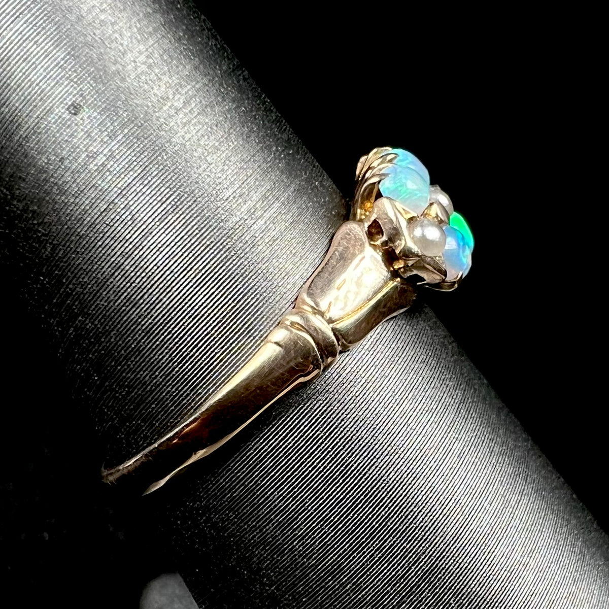 A 9k gold Victorian opal and pearl ring shown on ring display from side view, its polished shank in focus