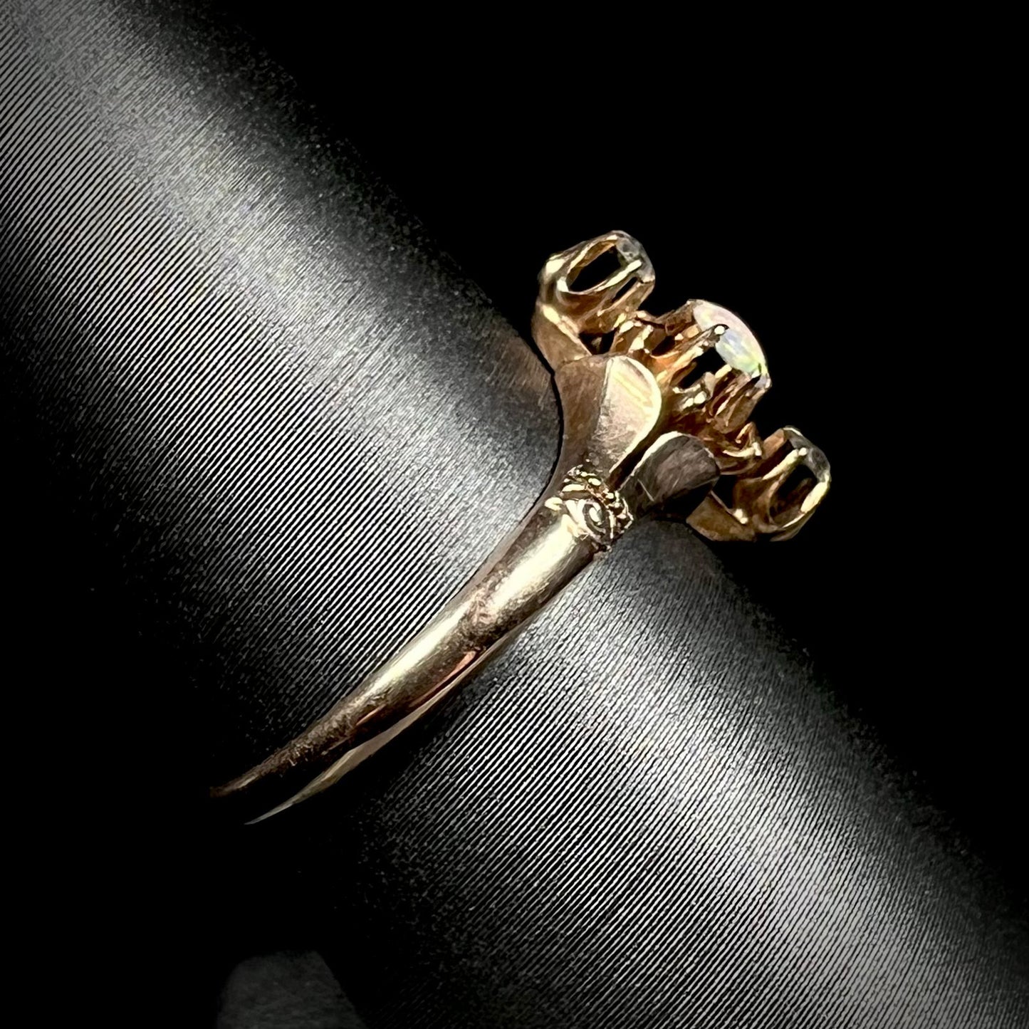 Side view of a 9k gold Victorian opal and diamond ring on a ring display against a black background.