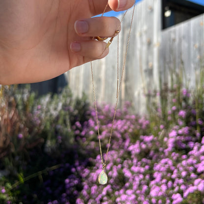 Adjustable opal necklace photographed outdoors against a bush with purple flowers. A small green flash is visible in the opal.