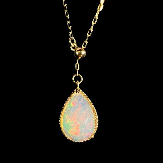 A dainty 10k gold adjustable opal necklace with a subtle red flash. The adjustable bead is visible above the opal.