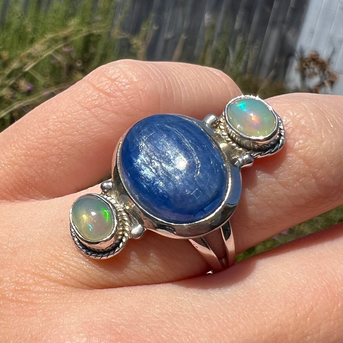 Angled sunlit view of the adularescence seen in a blue kyanite cabochon ring, worn on a finger.