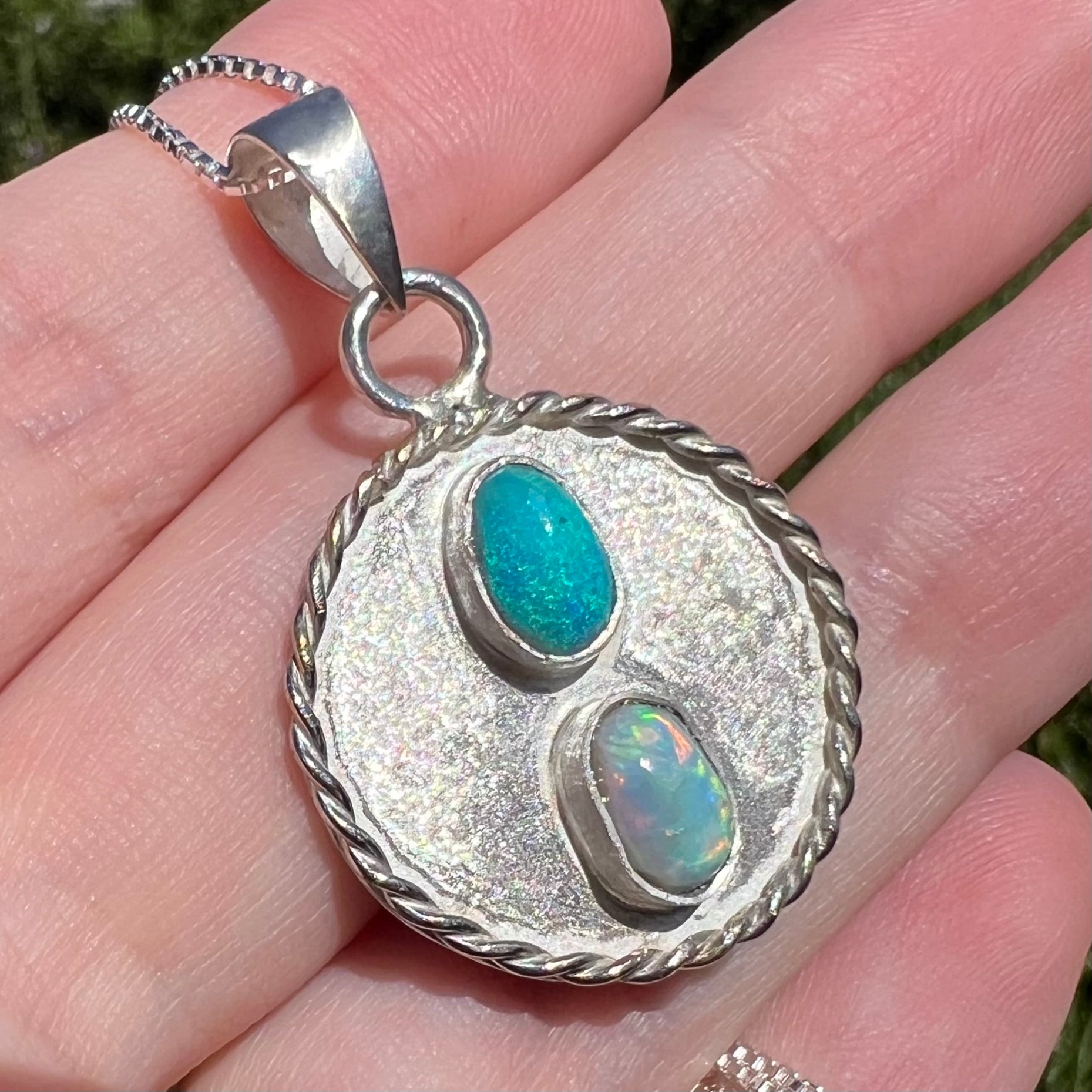 Angled close-up of an American-made sterling silver Australian opal men's pendant, shown in the sunlight held in a hand.