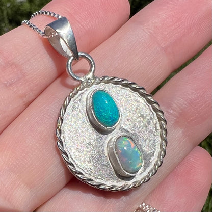 Angled close-up of an American-made sterling silver Australian opal men's pendant, shown in the sunlight held in a hand.
