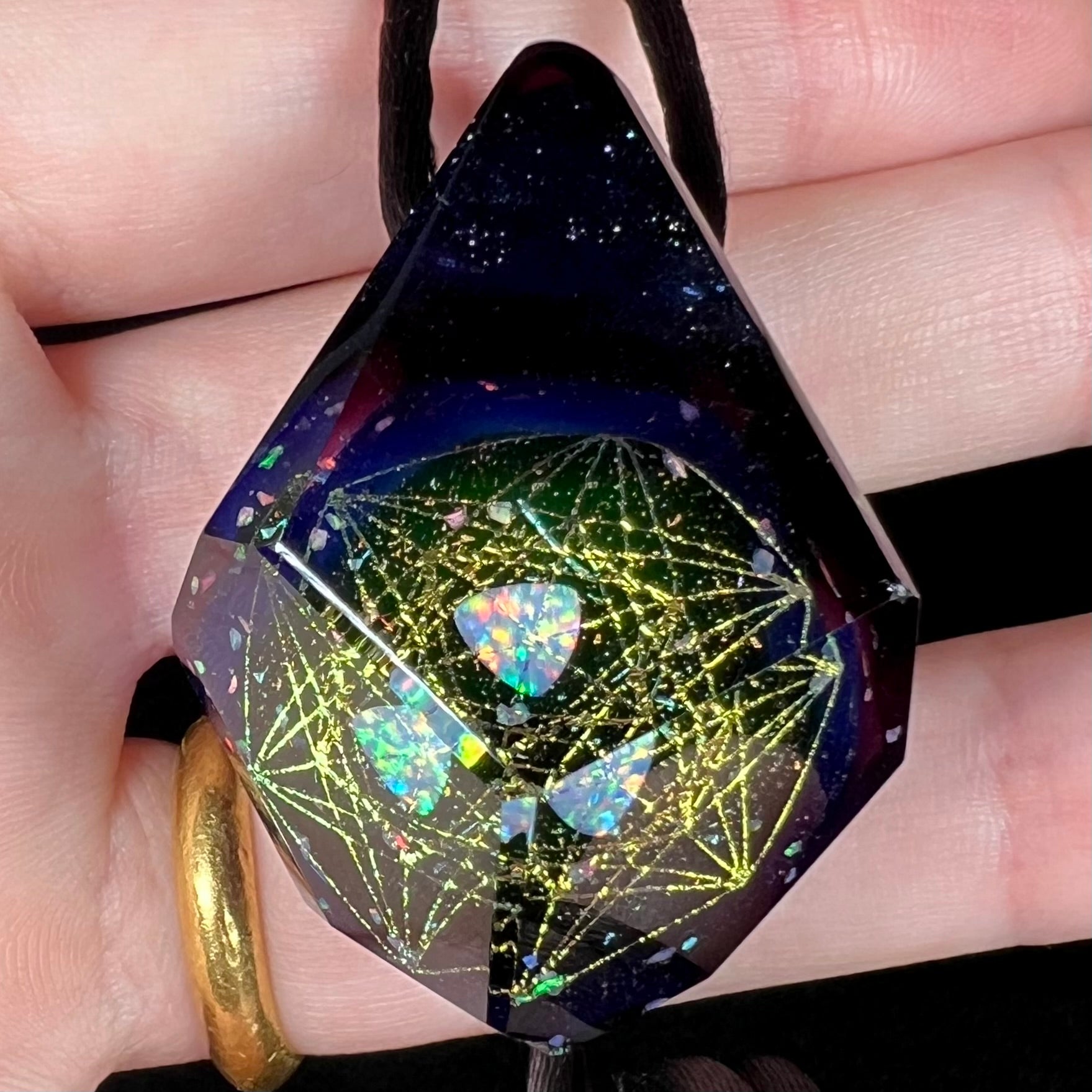A purple borosilicate amethyst glass and lab-created opal pendant shown close-up in a hand.  The opal reflects in multiple facets.