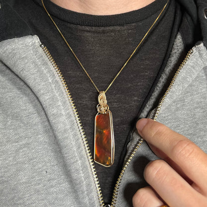 A gold filled wire wrapped ammolite necklace worn against a dark shirt in a partially unzipped jacket.