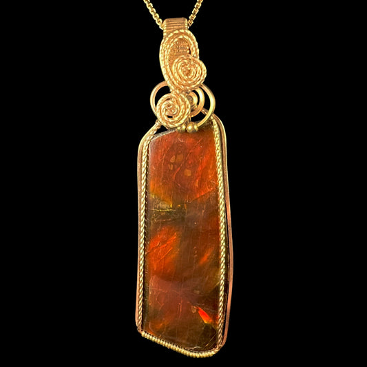 A gold filled wire wrapped ammolite pendant shown from the front against a black background.