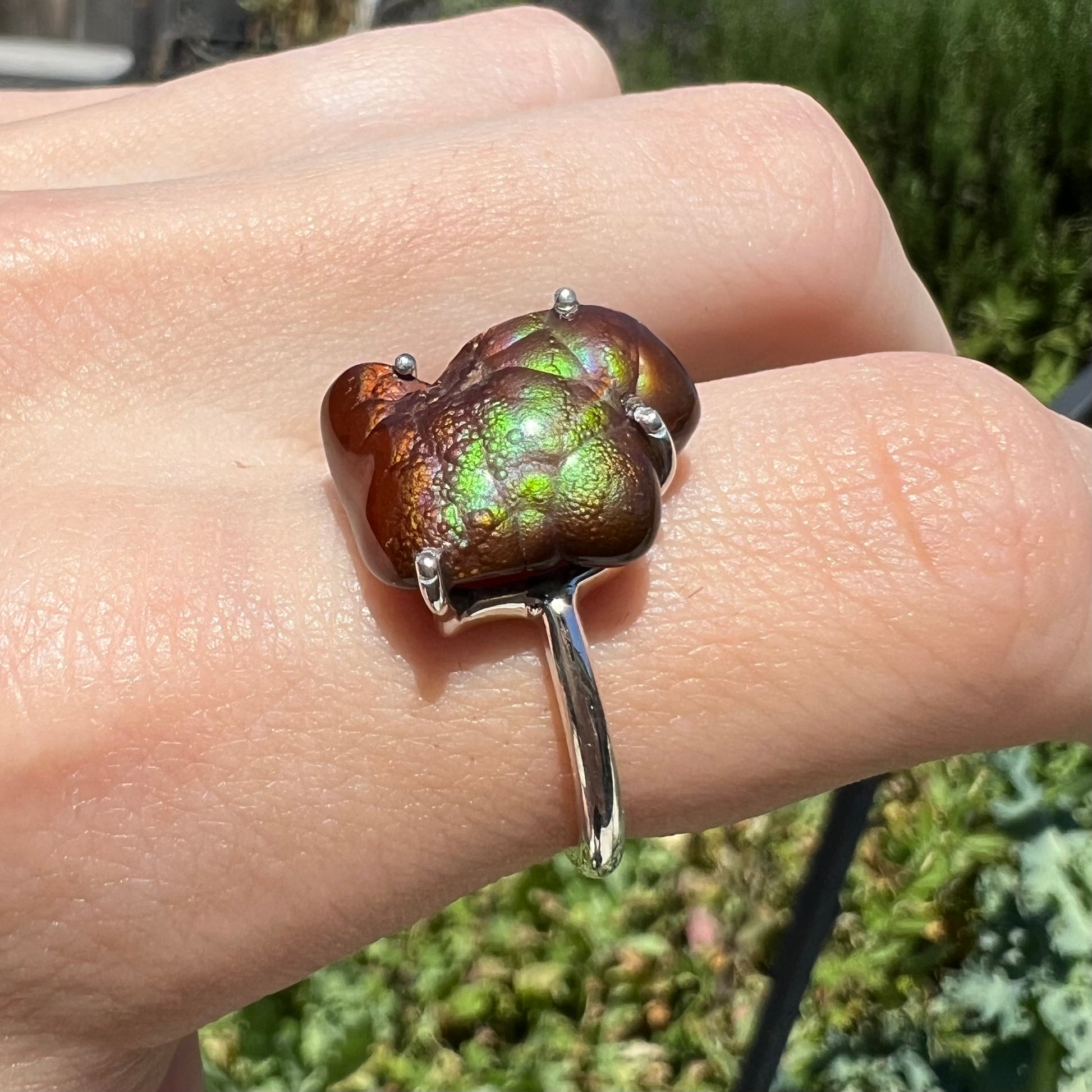 Angled view of fire agate ring in sunlight with green and subtle purple banding.