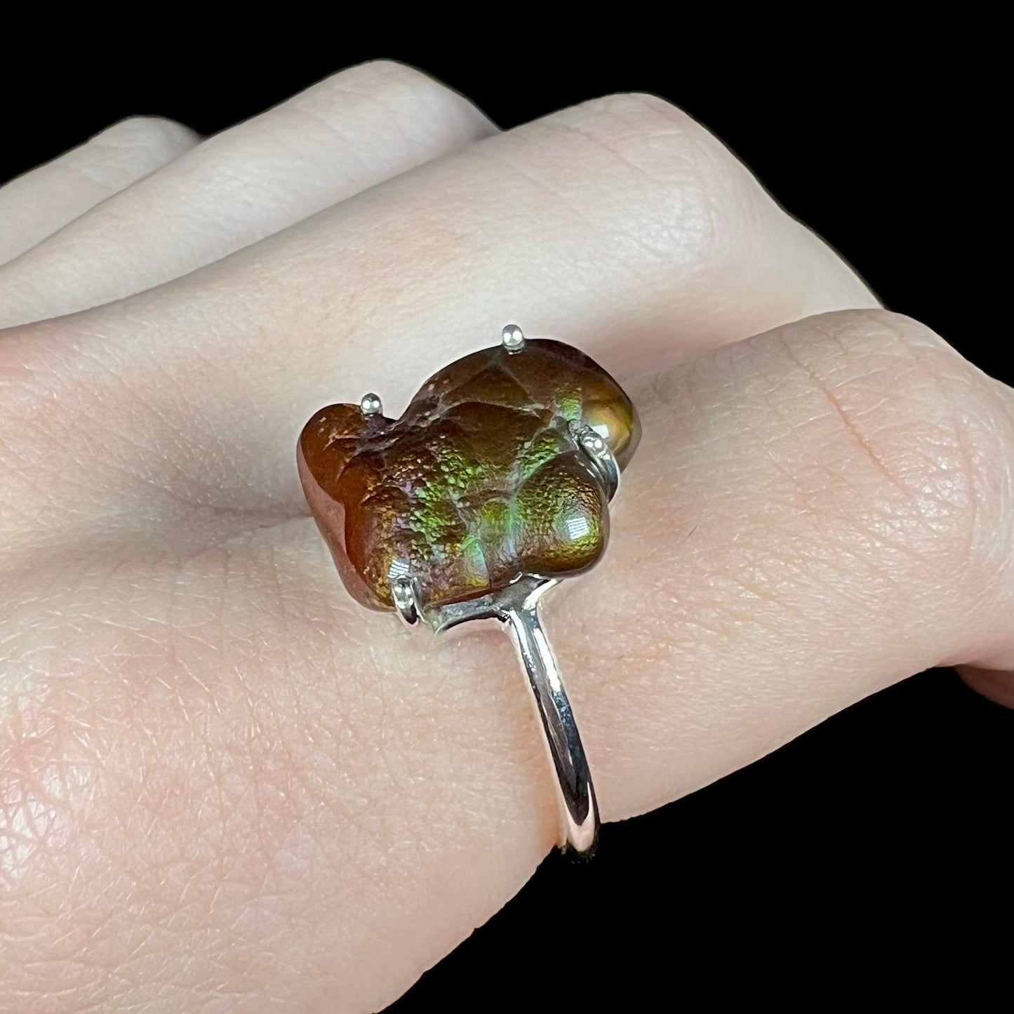 Angled macro shot of fire agate ring on fingers showing green stone with purple overtones.