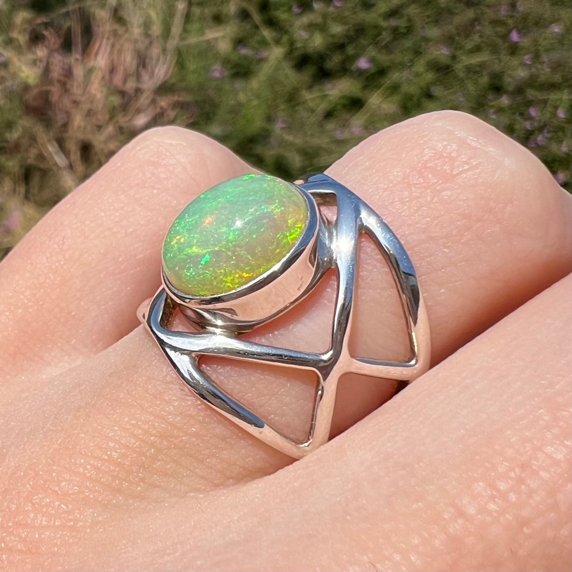 A silver opal ring with a wide, open design, worn on a finger and shown at an angle in natural light.
