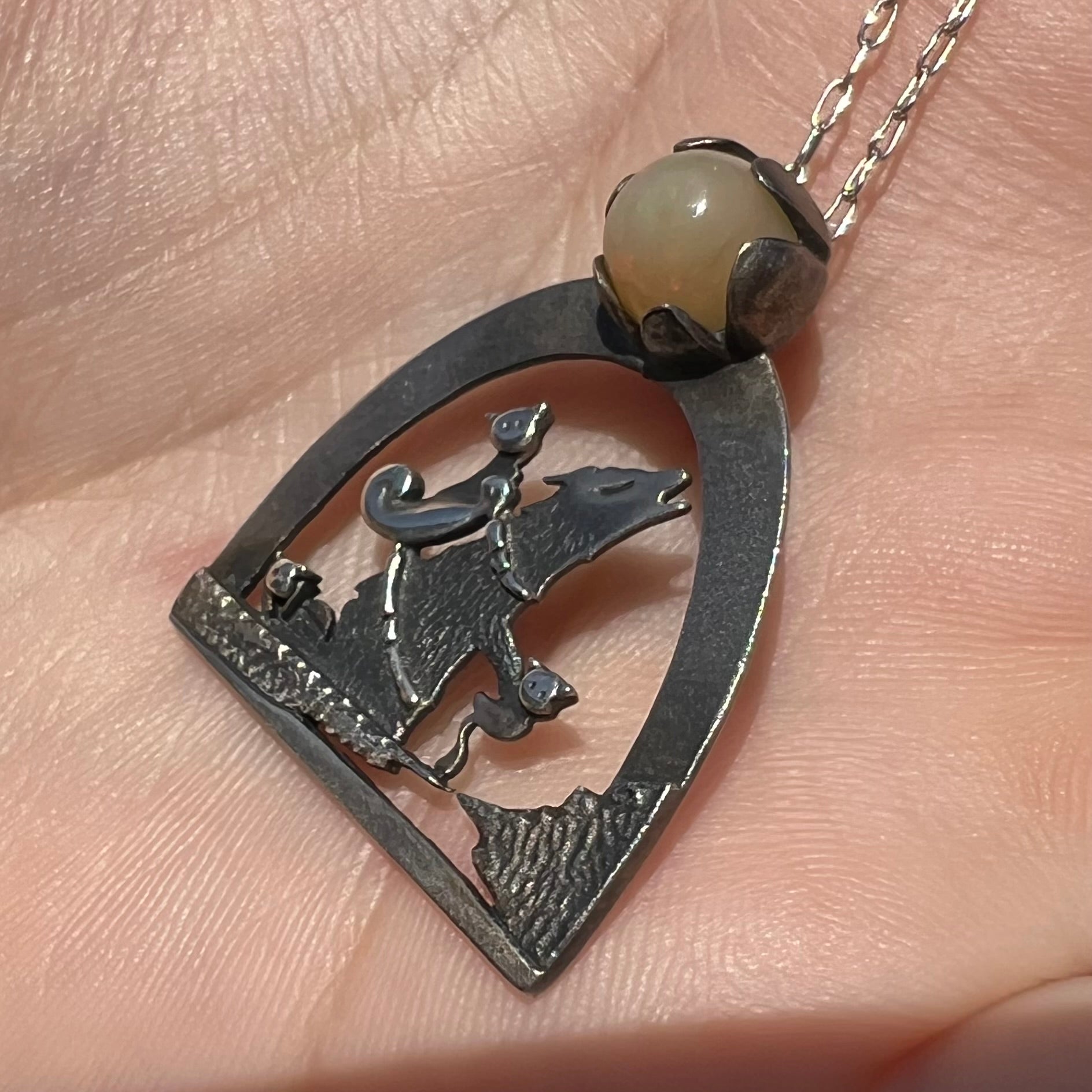 Close-up angled view of a sterling silver Ethiopian opal wolf and cat design necklace in sunlight against a hand.