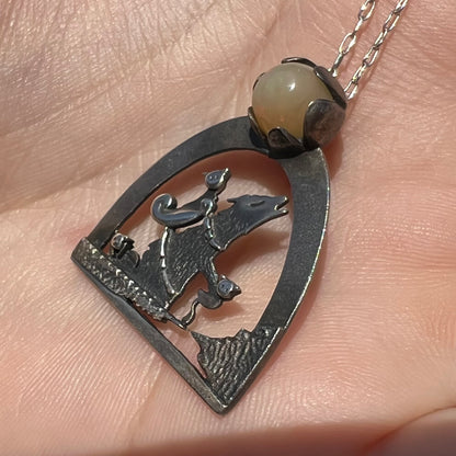 Close-up angled view of a sterling silver Ethiopian opal wolf and cat design necklace in sunlight against a hand.