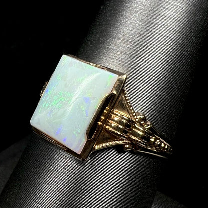 Angled close-up of an antique c.1920s era Art Deco opal solitaire ring in 10k gold on a ring display, focused on ring's ornate milgrain-textured shoulder