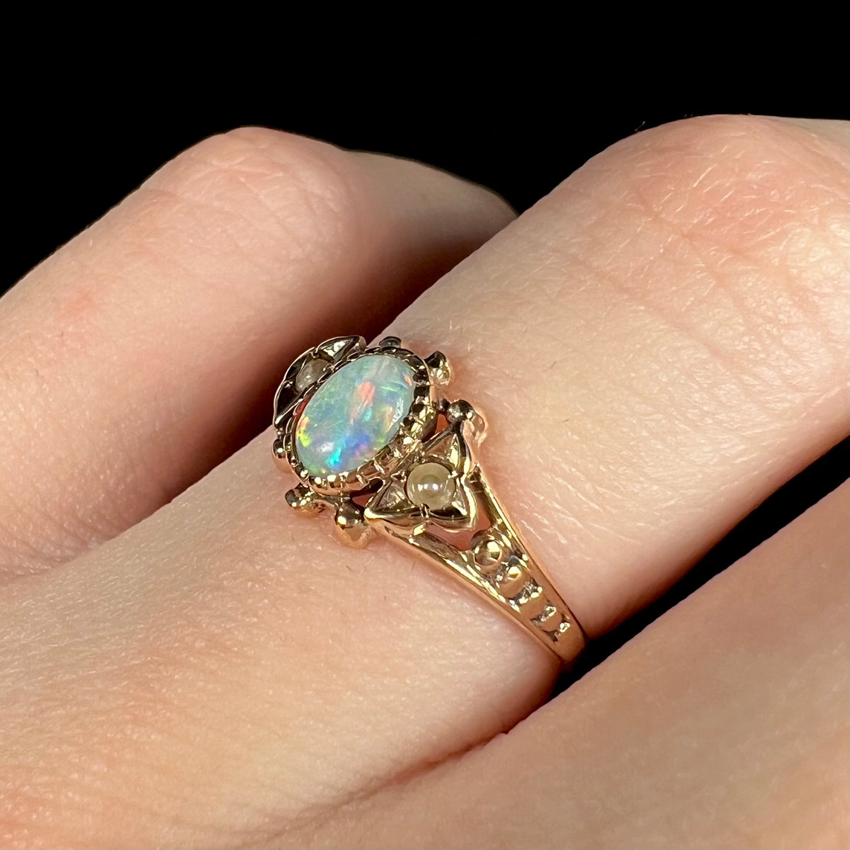 Angled close-up of antique 1890s era 9k gold Australian opal ring, focusing on ornate design and seed pearl accent
