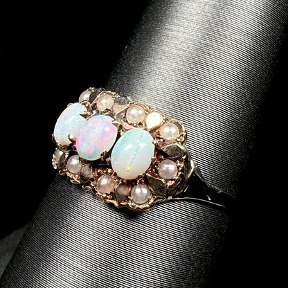 Angled close-up of antique 9k gold three-stone opal ring with halo of seed pearl accents, shown on ring display