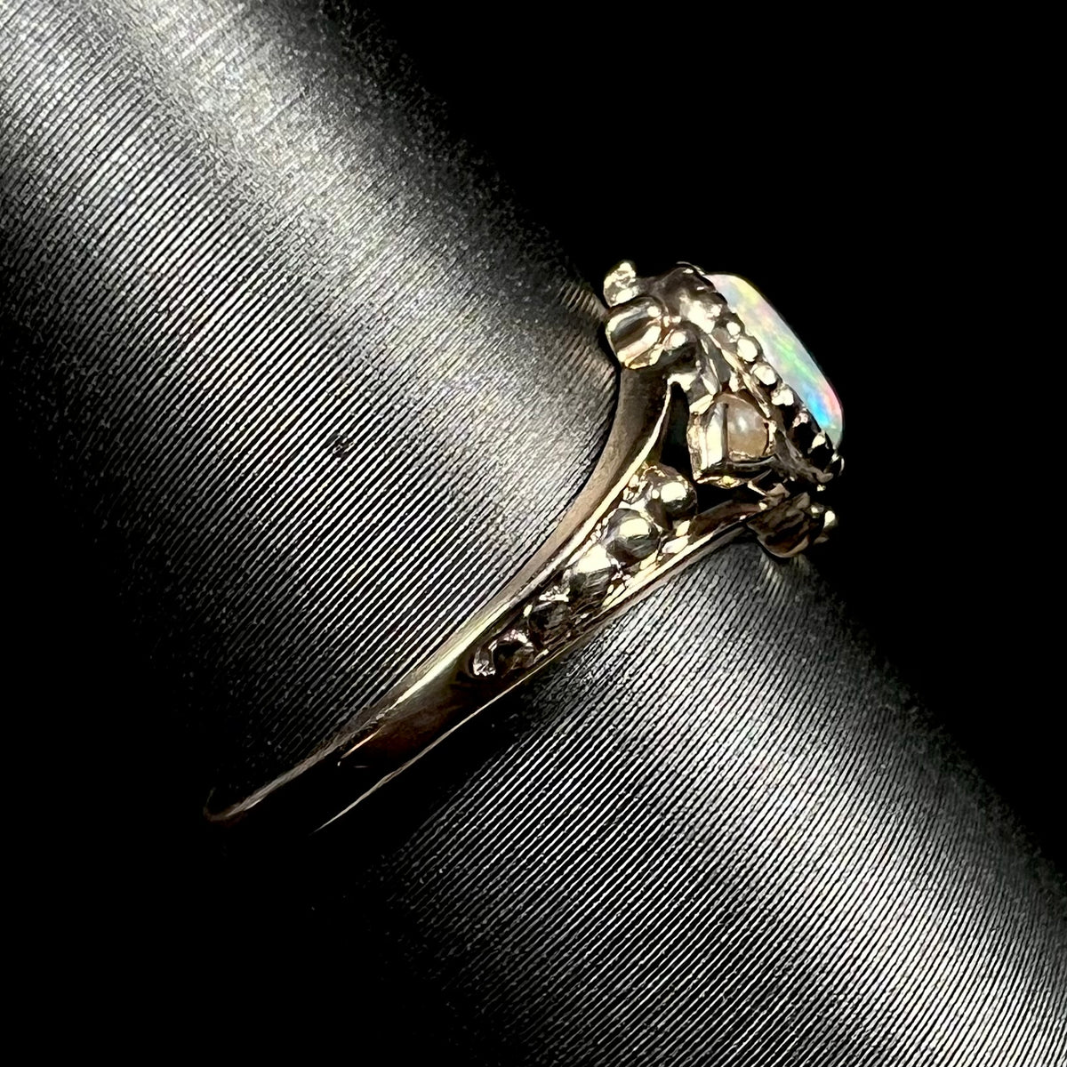 An antique 9k gold opal and pearl ring on ring display shown from the side view, focused on ring's dainty shank