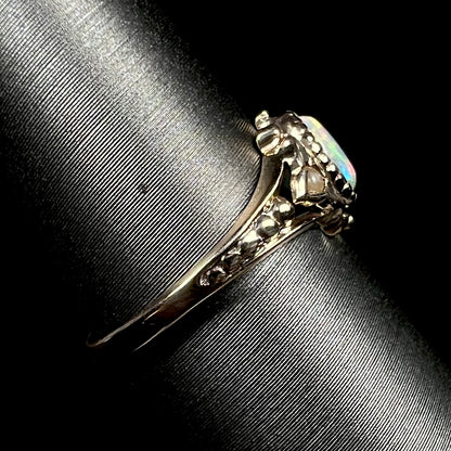 An antique 9k gold opal and pearl ring on ring display shown from the side view, focused on ring's dainty shank