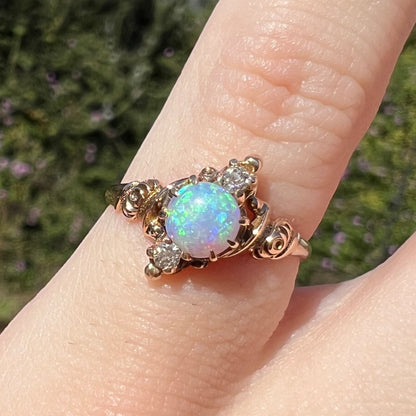 Close-up of Art Nouveau era opal and diamond pinky ring, worn on finger in sunlight; the opal shows green and blue colors