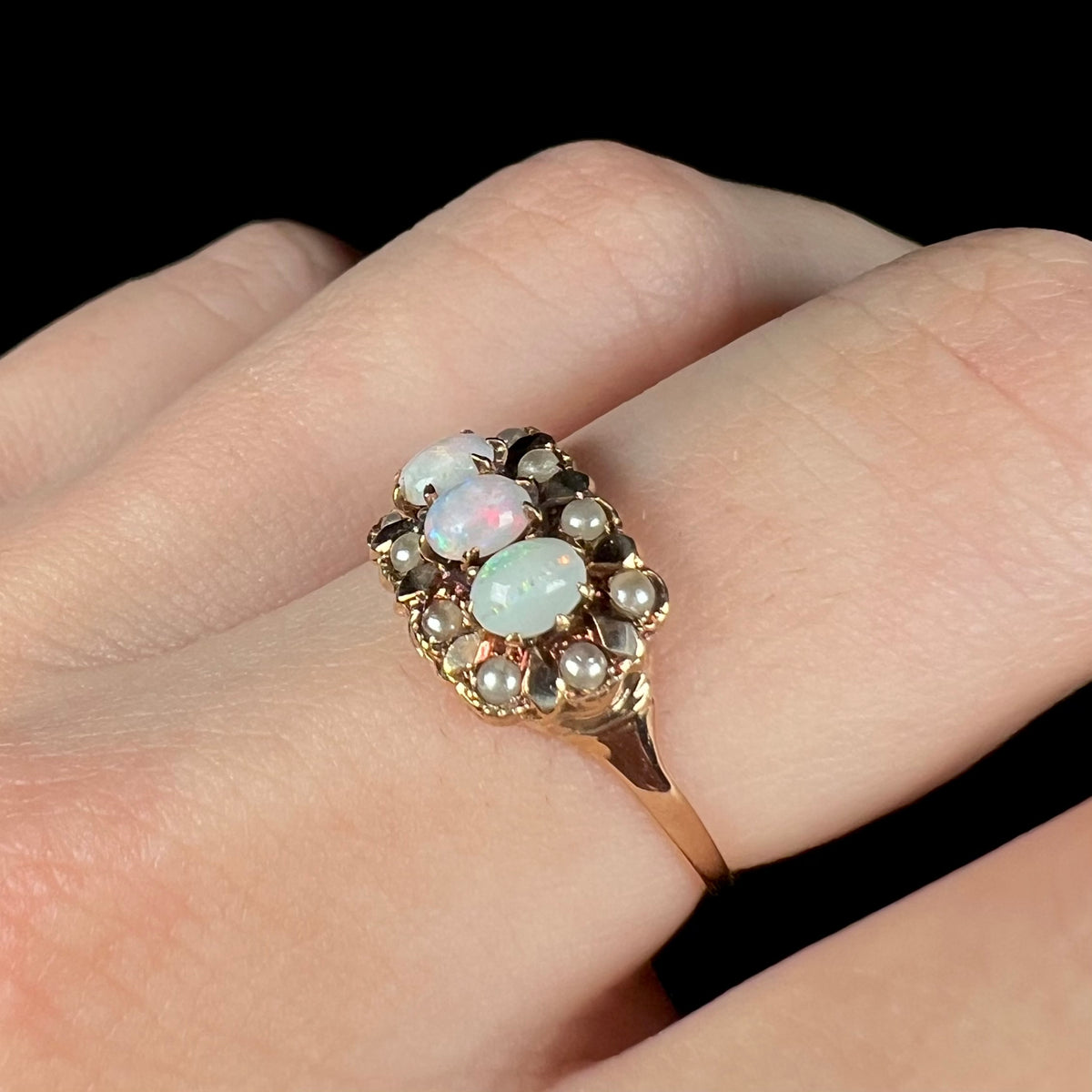 Angled close-up of finger wearing antique Australian opal and seed pearl ring in gold