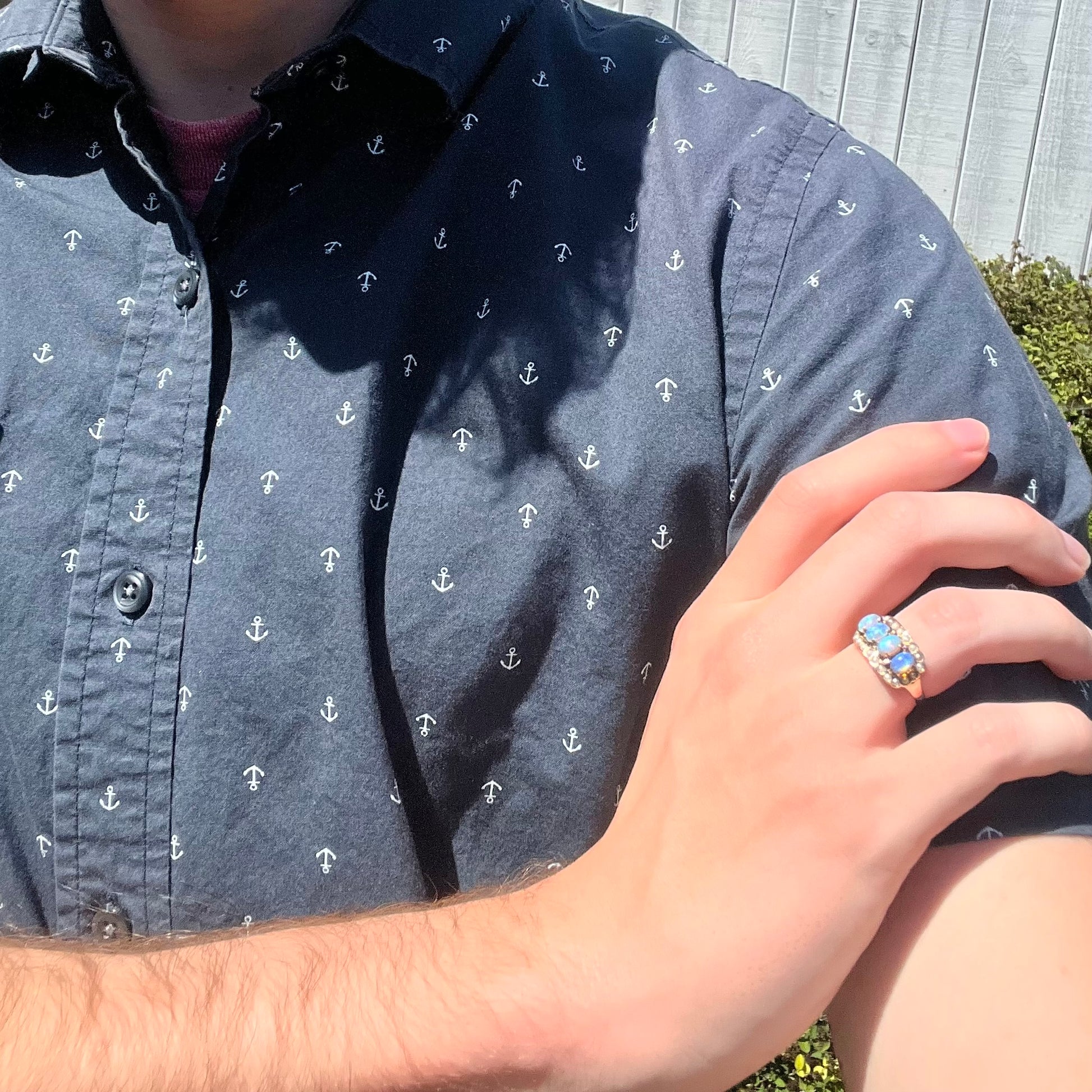 Close-up of person resting hand on opposing shoulder wearing antique 9k gold crystal opal ring in sunlight