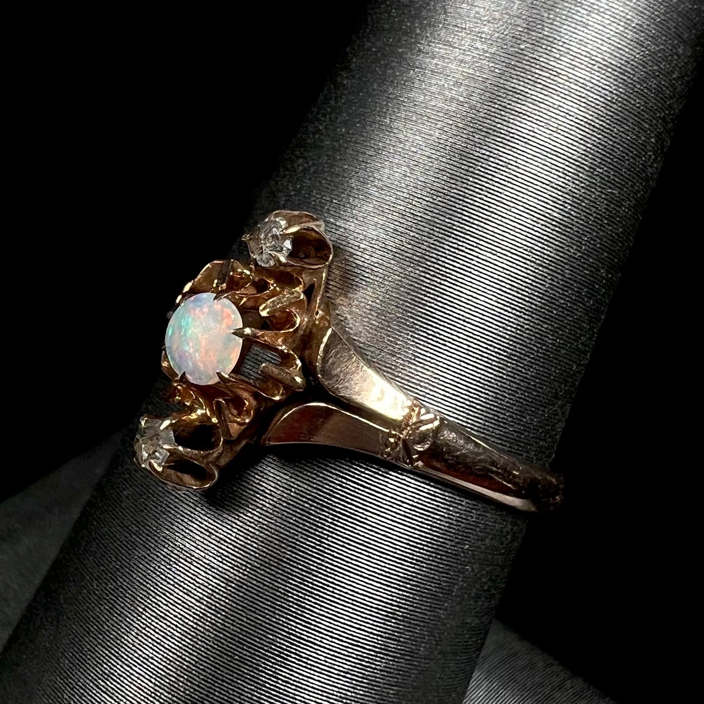 An antique English three-stone opal and rose cut diamond ring shown close-up from an angle on a ring display against a black backdrop.