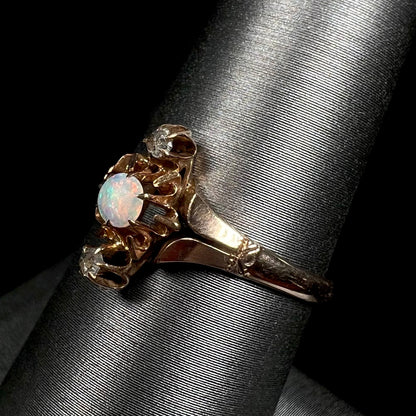 An antique English three-stone opal and rose cut diamond ring shown close-up from an angle on a ring display against a black backdrop.