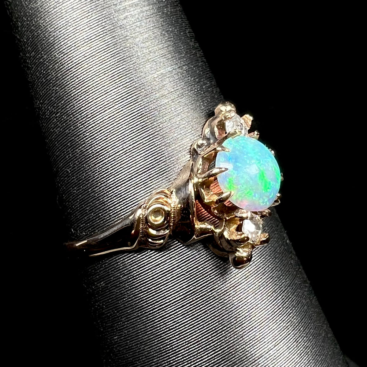 A turn of the 20th century antique opal and diamond ring, shown on a ring display close-up from angle; a floral motif is seen in ring's 10k gold shoulder