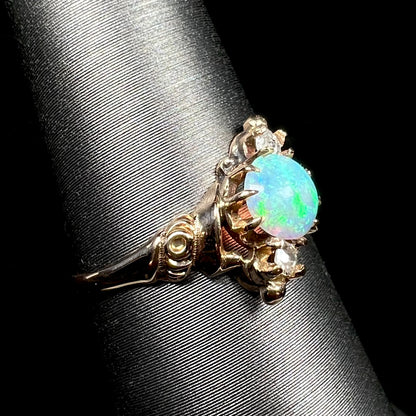 A turn of the 20th century antique opal and diamond ring, shown on a ring display close-up from angle; a floral motif is seen in ring's 10k gold shoulder