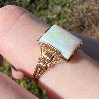 Side view of an antique 10k gold rectangle-shaped opal ring with an Art Deco design, worn on a finger in sunlight