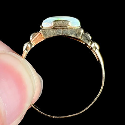 Close-up showing full side profile of antique 10k gold Art Deco opal ring, held from the side of its shank between two fingers