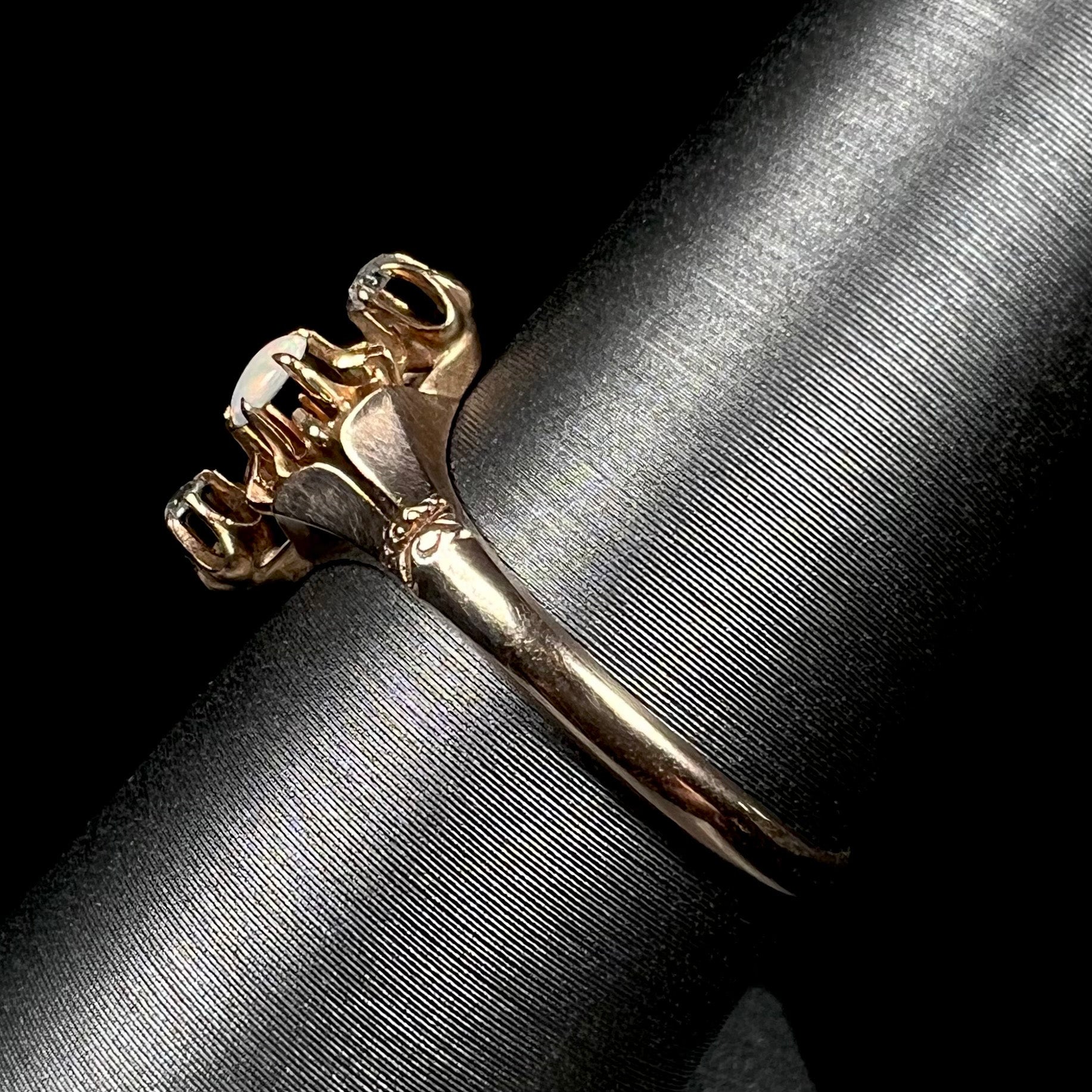 An antique English three-stone opal and diamond gold ring shown close-up from the side view on a ring display against a black background.