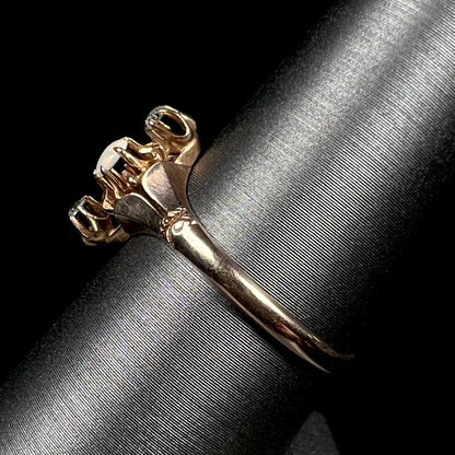 An antique English three-stone opal and diamond gold ring shown close-up from the side view on a ring display against a black background.