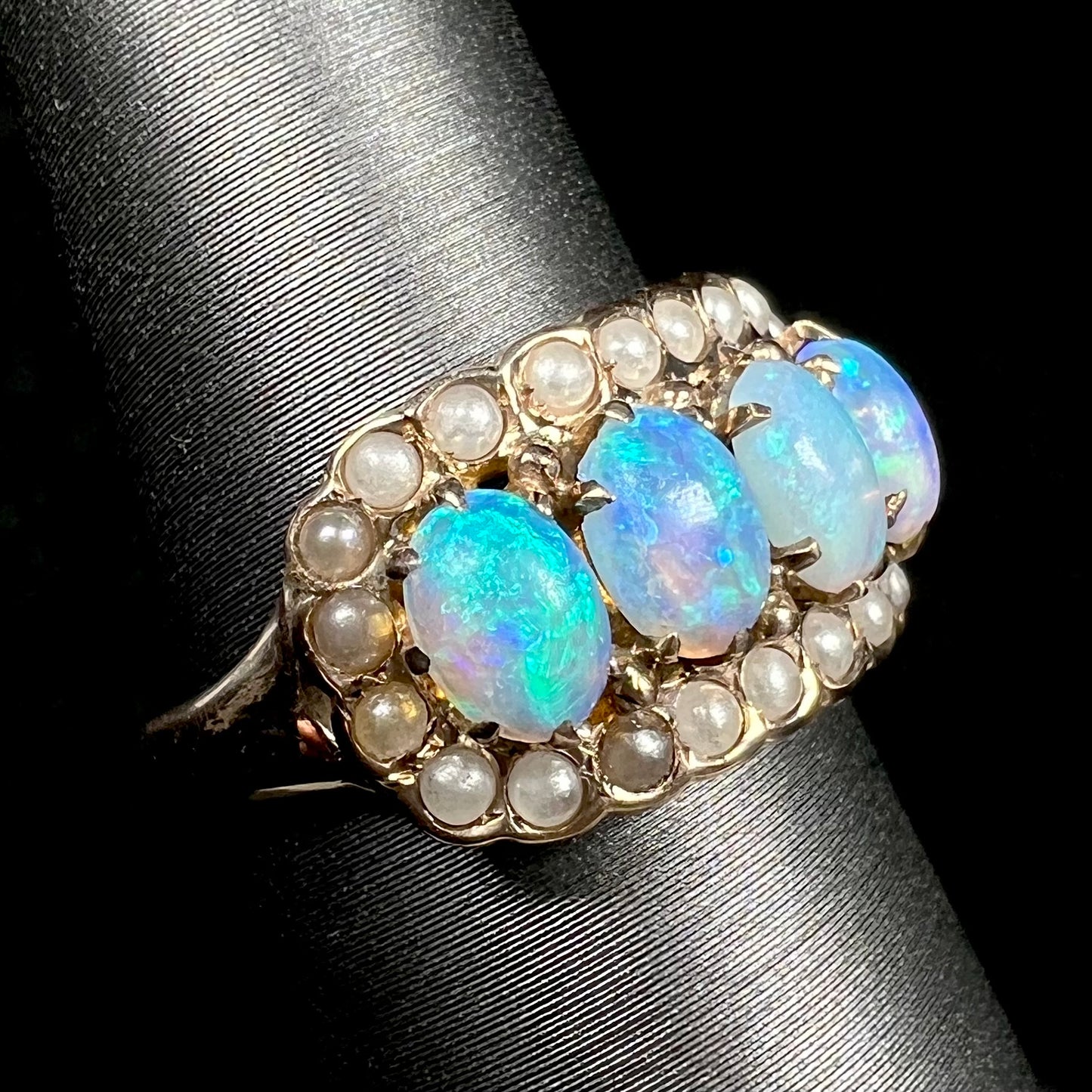 Antique 1880s ring set with four blue Hungarian crystal opals inside of a seed pearl halo, shown from angle on display