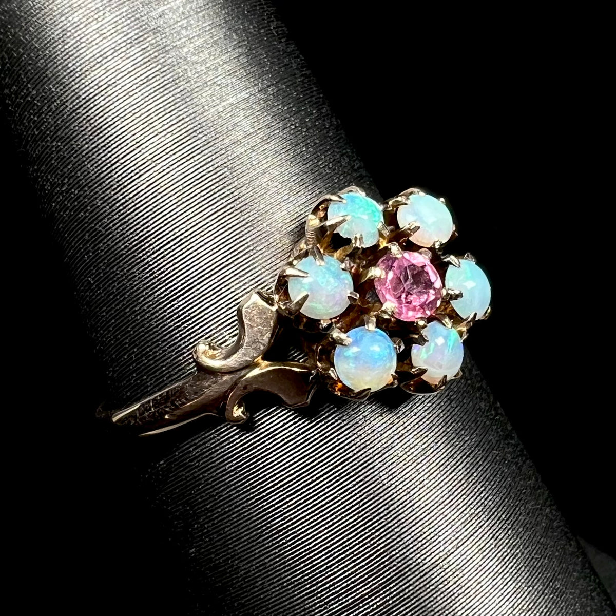 Antique 9k gold ring set with six round Hungarian opals and a pink tourmaline center stone, shown on ring display