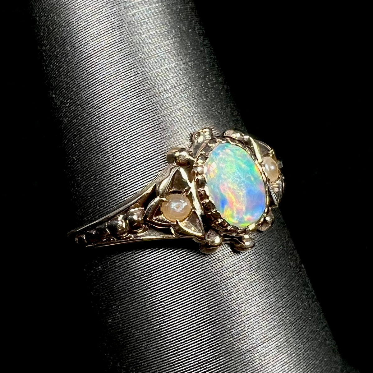 An antique 9k gold opal and seed pearl engagement ring from the late Victorian era, shown on ring display from close-up angle