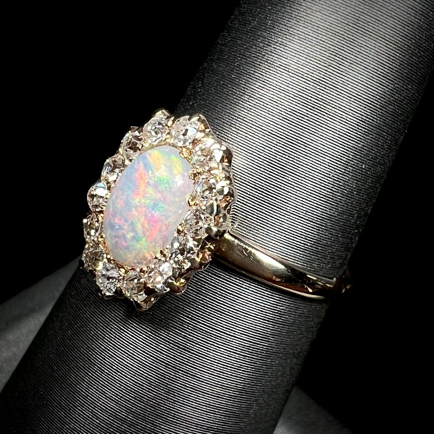 The side angle of an Edwardian opal diamond halo ring.  The opal has soft pink and green colors.