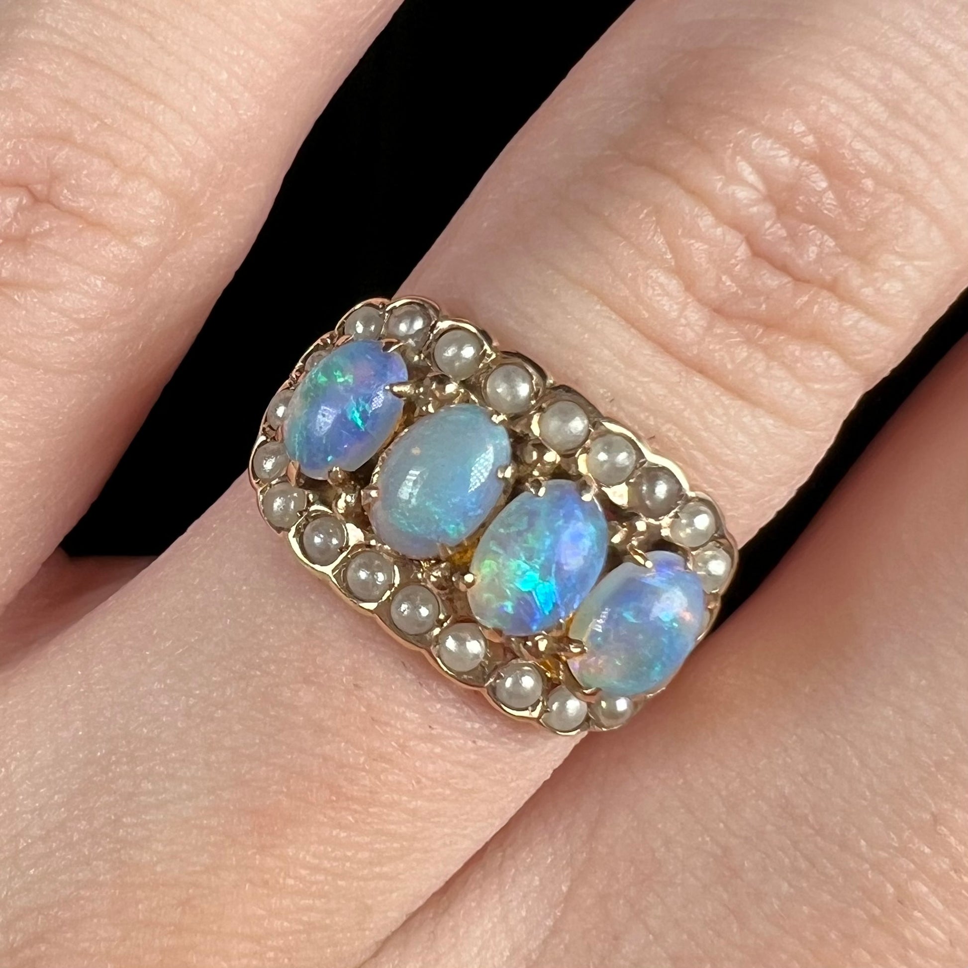 Macro close-up of antique four-stone opal and seed pearl halo ring, worn on finger